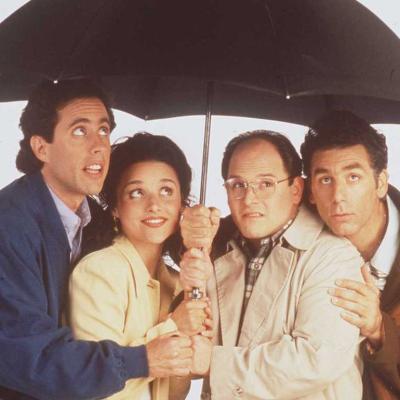 Actors Jerry Seinfeld, Julia Louis-Dreyfus, Jason Alexander, and Michael Richards pose for a promotional photo for 'Seinfeld' under an umbrella.