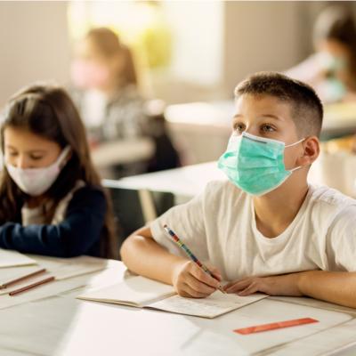 Two elementary students taking a test in their classroom while wearing protective face masks