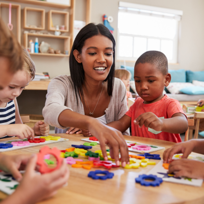 A teacher working with young students at a table in a classroom.