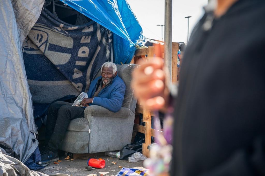 Ashby Dancy sits in an upholstered gray recliner chair in his tent while looking toward his grandson Mekhi Terrell who is not in the photo.