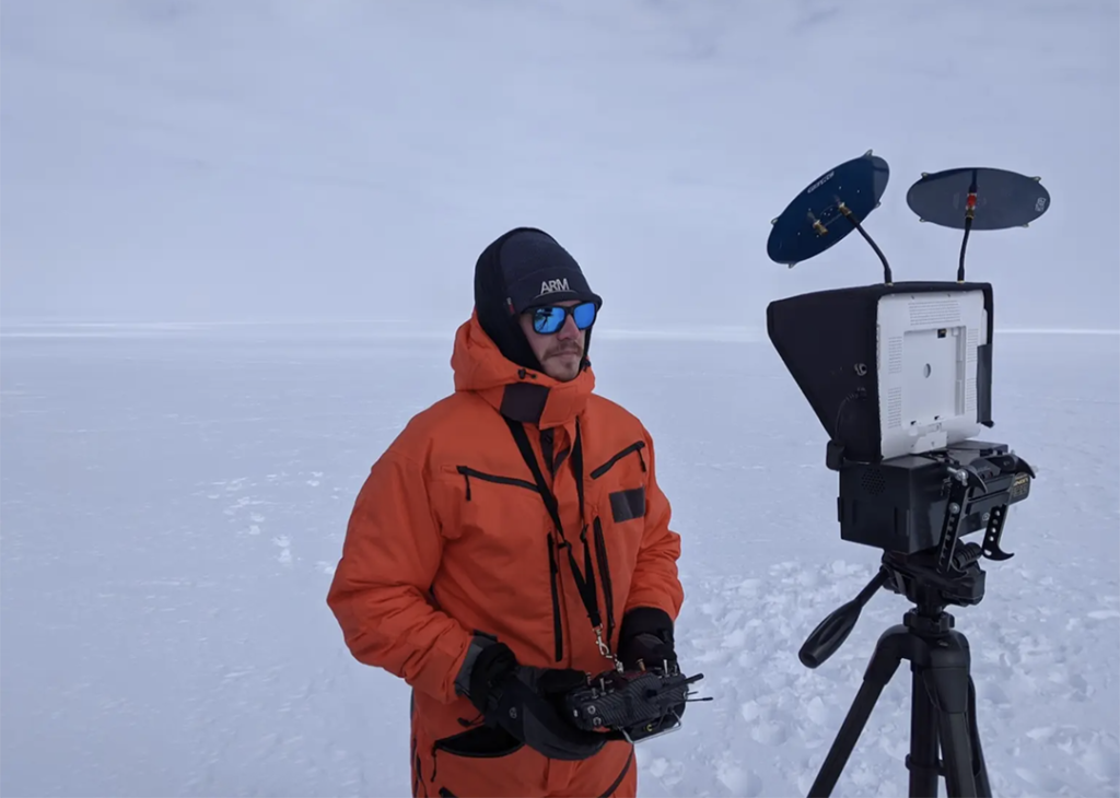 Matthew Boyer in an orange jacket pilots a data-collecting drone while standing on a sheet of ice and snow.