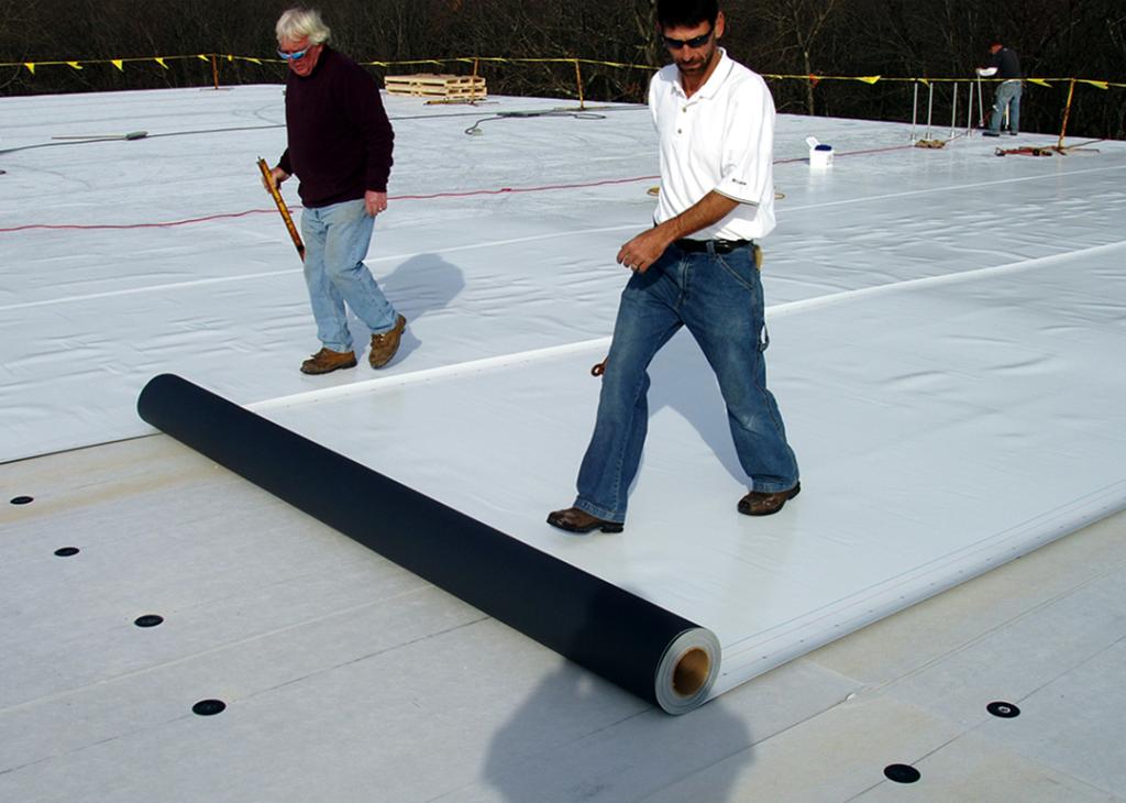 Workers lay down white PVC roofing material on a commercial building in Massachusetts.