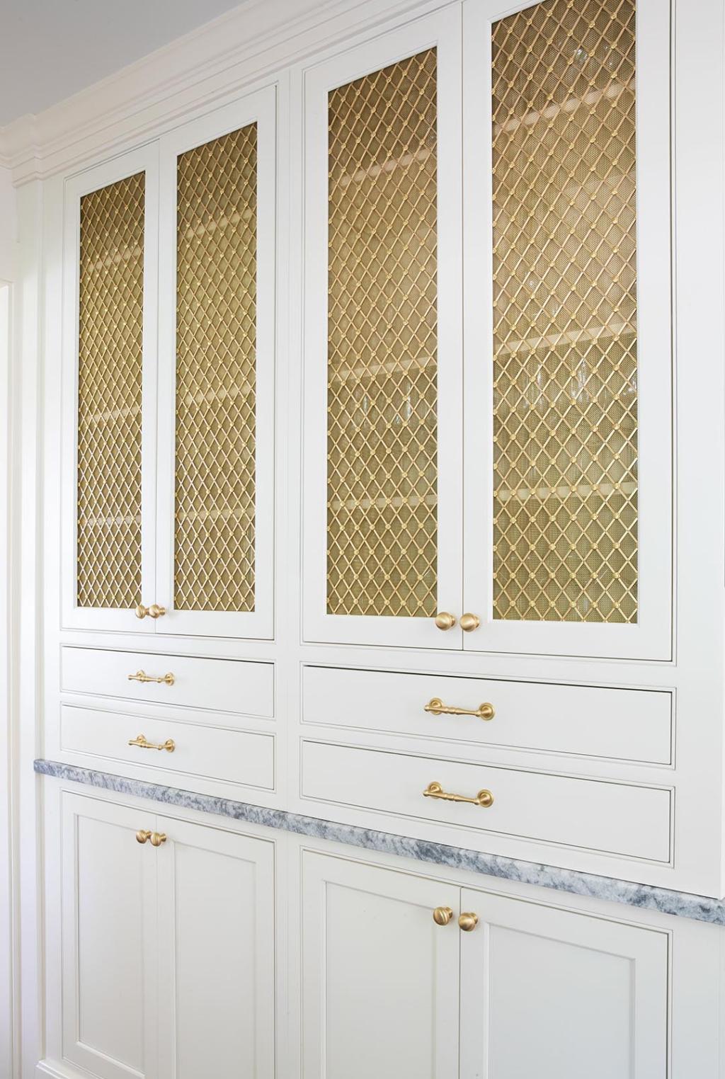 Kitchen cabinets known as the "appliance garage" have a gold lattice front that allows visibility into what is inside.