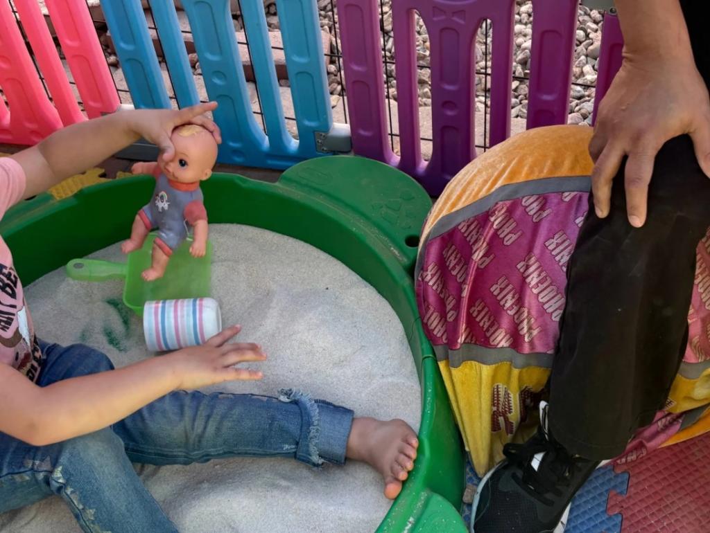 A child plays with a doll in a sandbox in the child care facility's back yard.