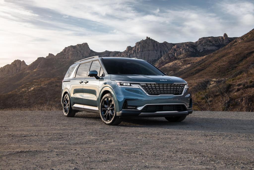 A blue 2024 Kia Carnival minivan parked outside in nature.