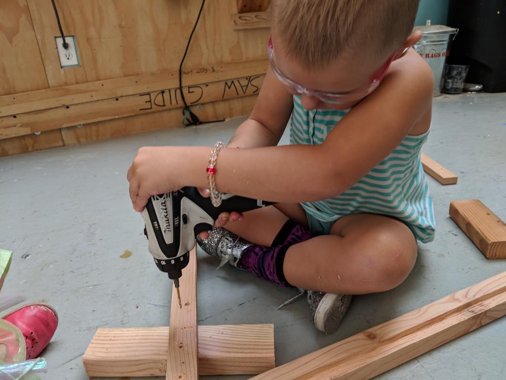 A young girl working a drilling tool into wooden planks.