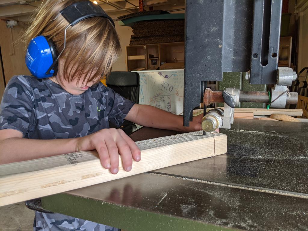 A young boy cuts wood with a vertical saw machine.