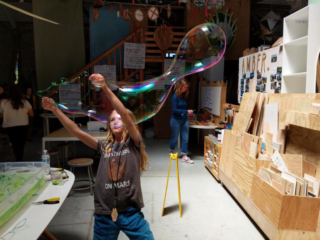 A young girl testing a giant bubble wand made from pieces of special ropes.