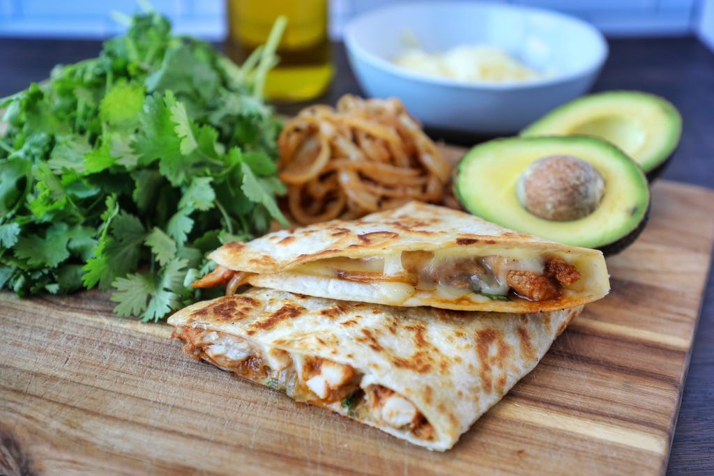 Chicken shawarma quesadillas served with fresh herbs, caramelized onions, and avocado halves.
