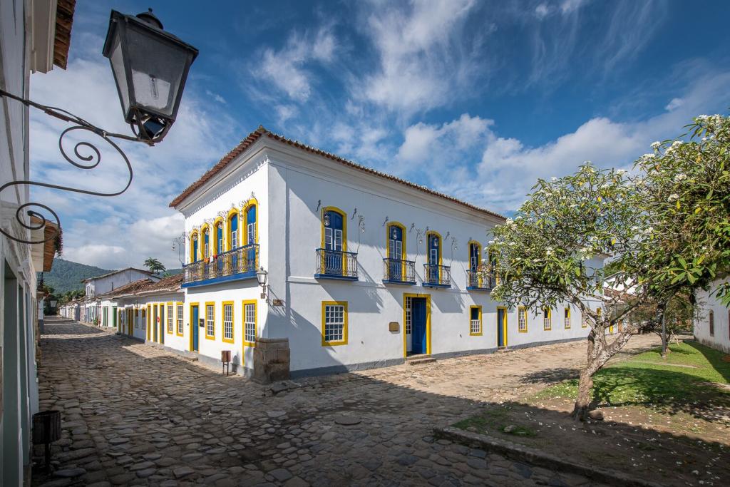 View of the exterior of Sandi Hotel, a charming white building on a cobblestone street, with blue sky and clouds above.