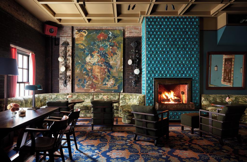 View of lobby of the Nine Orchard Hotel featuring richly-colored tapestries and walls with bold accents, dark mahogany furniture and a blazing fire.