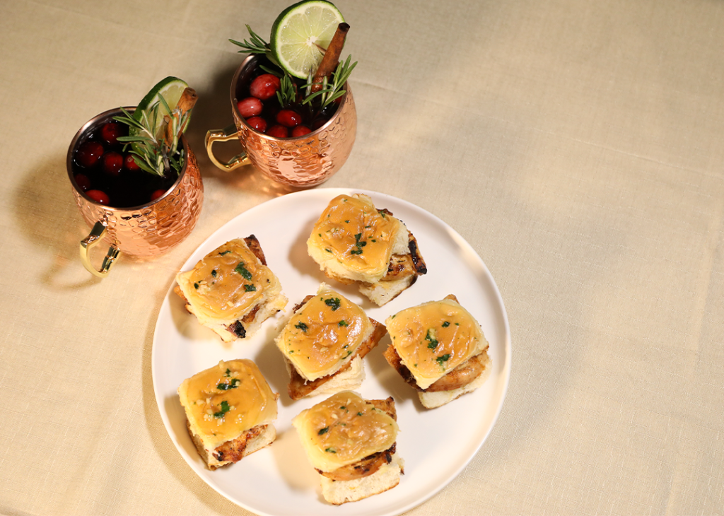 A plate of Hot Honey Grilled Chicken Sliders and two pints of Cranberry Mule drinks.