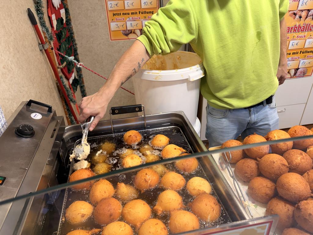 A vendor fries Quarkbällchen, small fried dough balls made with soft cheese.