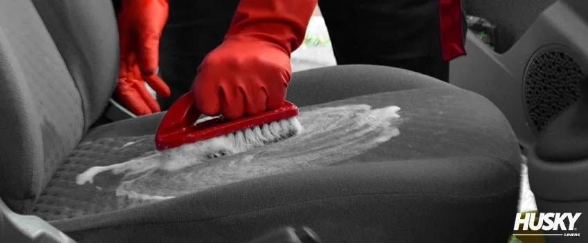 A detailer cleaning the upholstered seat of a car with soap and brush.
