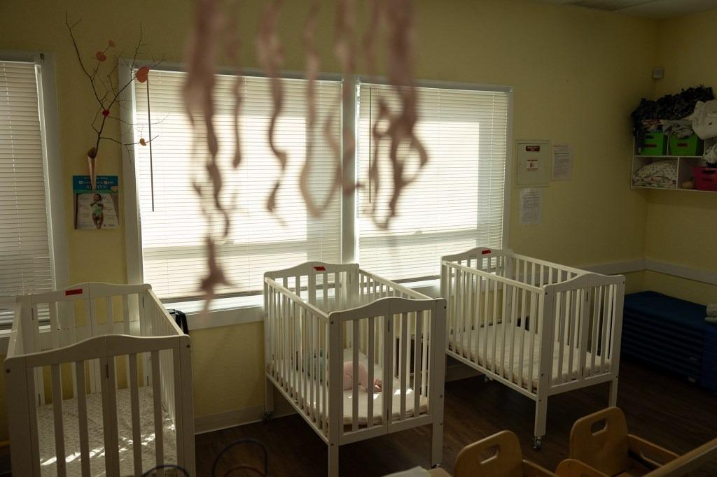 Three baby cribs with a child in the middle one, in front of closed blinds to block out the sun at Moore Learning Preschool & Childcare Center in Elk Grove.