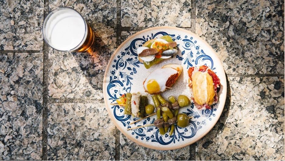 A plate full of assorted of tapas with a glass of beer on the side.
