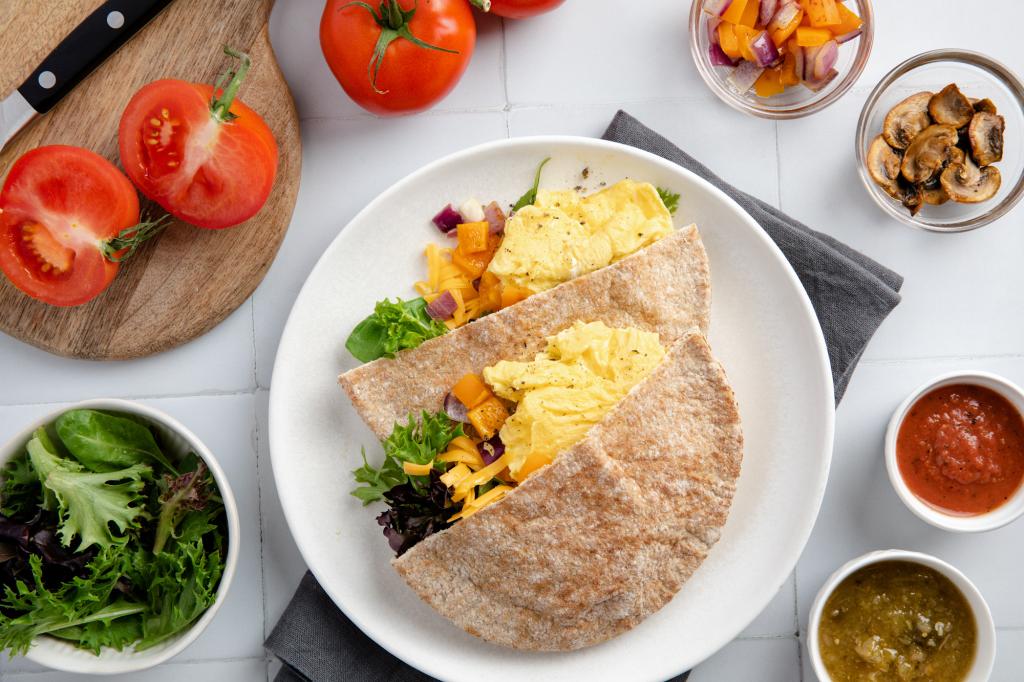 Top-down view of egg-stuffed pitas with optional topings like tomatoes and mushrooms.