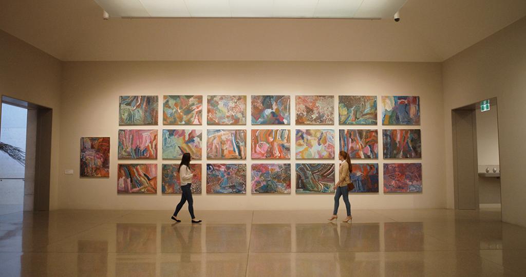 Two visitors walk by a wall where 22 canvases of paintings from "The Alhalkere Suite" by Emily Kam Kngwarray are displayed at the national gallery in Canberra.