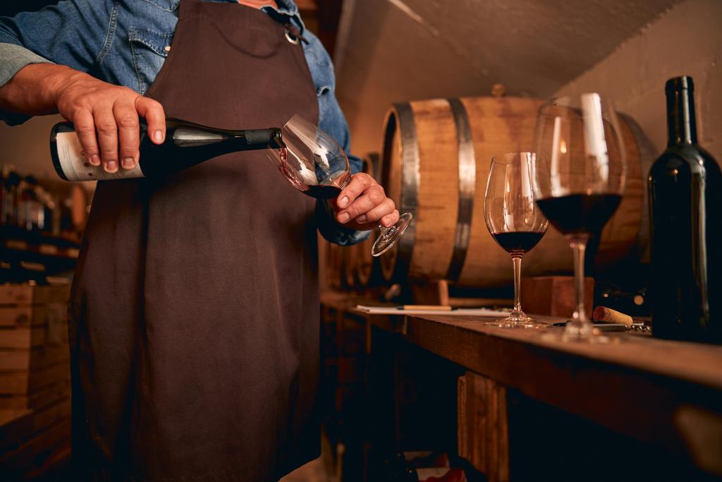 A sommelier pouring red wine into a glass.