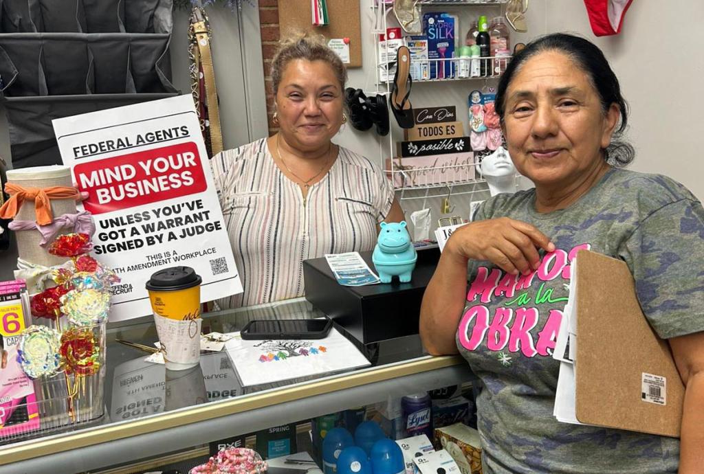 Two people standing at a counter showing the 4th Amendment Workplaces signage for their business.