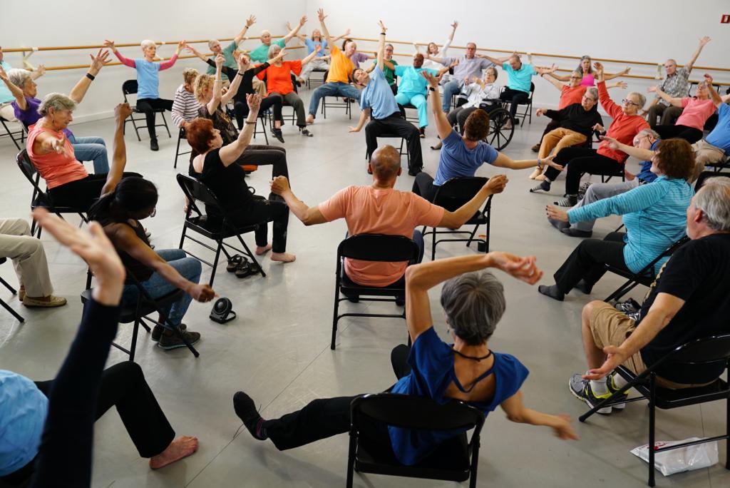 High-angle view of a room full of people dancing while in folding chairs.
