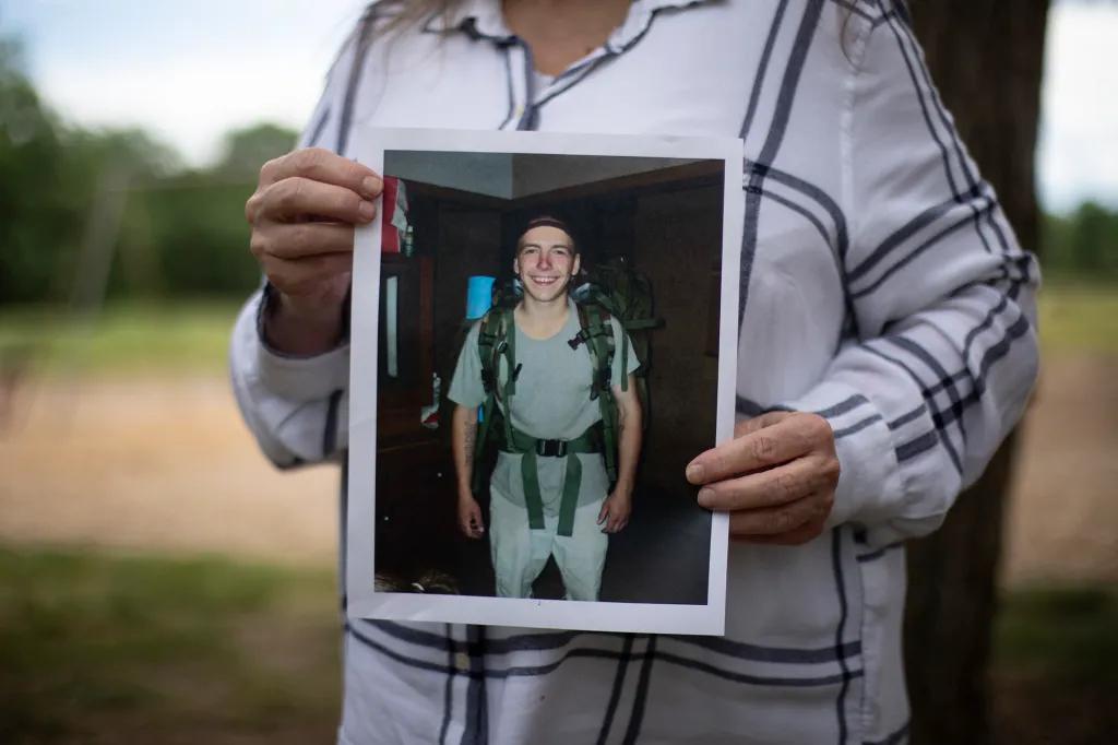 A photo of David Couch wearing a gray t-shirt, light pants and a backpacking pack smiling at the camera, the photo is in the hands of his mother Jeanelle Couch who is standing in Cascade Park in Redding on April 8, 2026.
