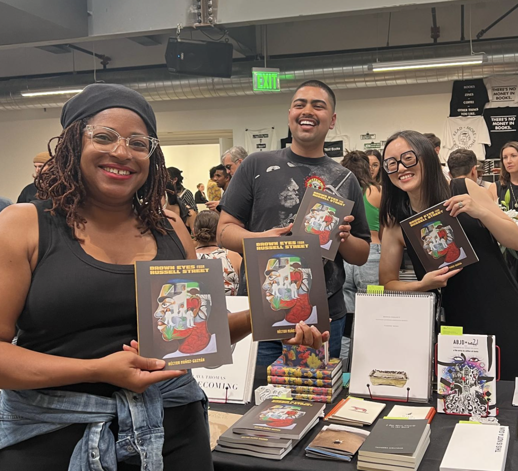 Three people holding up the book "Brown Eyes on Russell Street" at the San Francisco Art Book Fair.