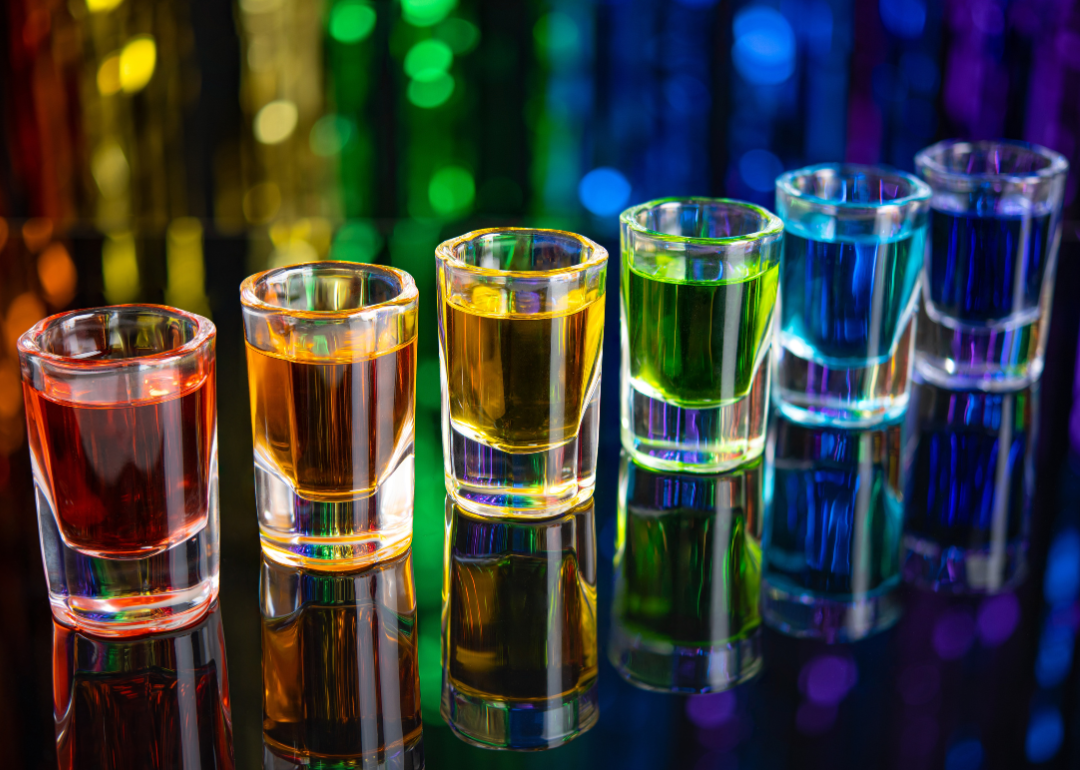 A rainbow of shot glasses on a bar.