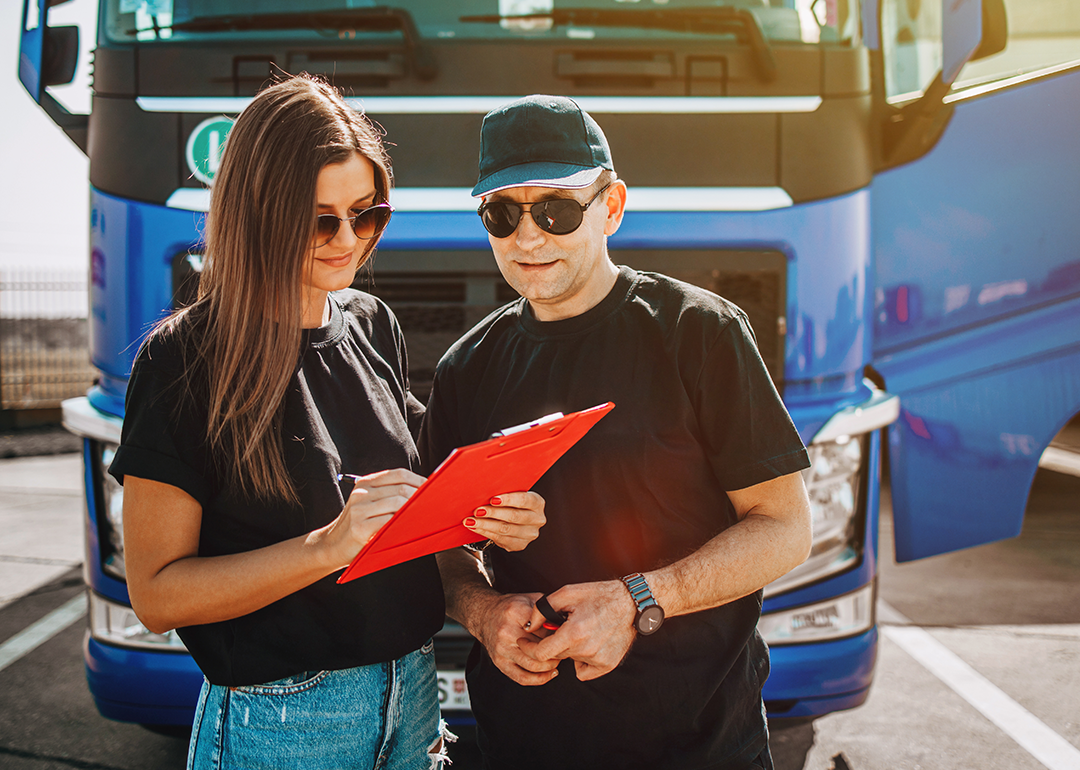 Two truck drivers review clipboard in front of semi truck.