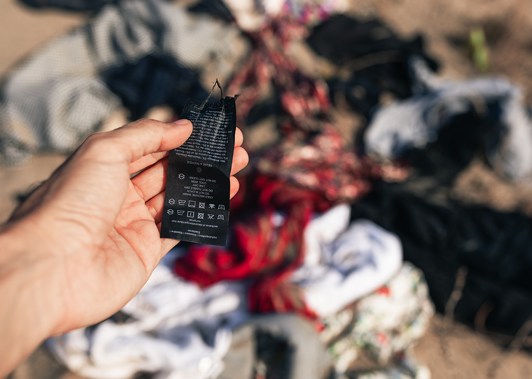 Hand holding clothing tag with textile waste in background.