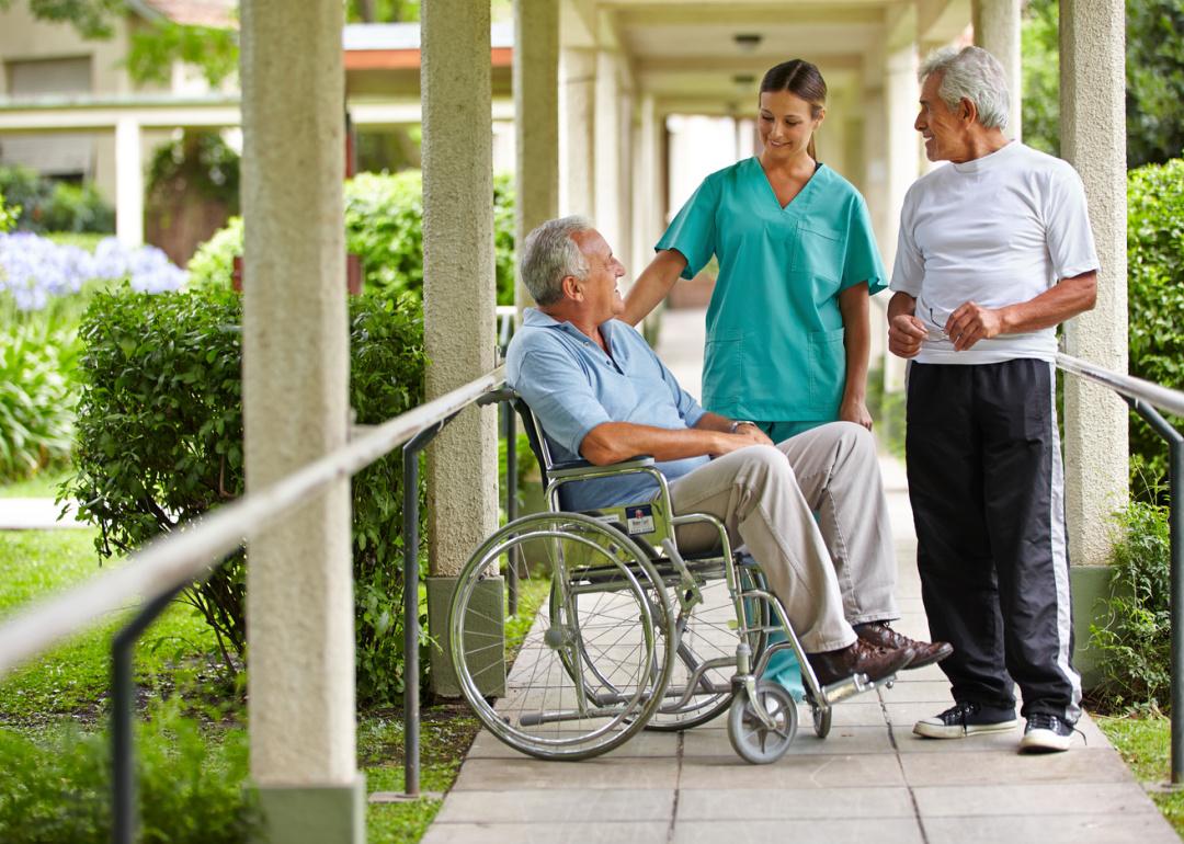 Two seniors talking to a nurse in the garden of a nursing facility.