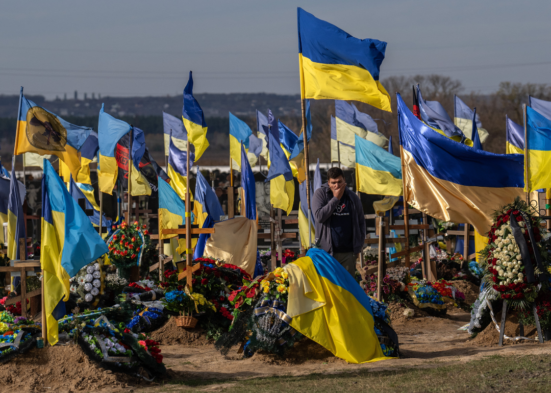 A man pauses by a grave as Ukrainian flags fly in a cemetery for soldiers killed in action.