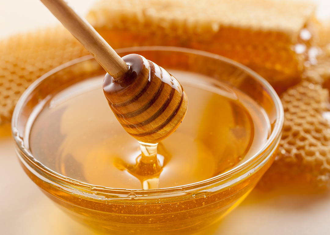 Closeup honey dripper, glass bowl of honey, and honeycomb.