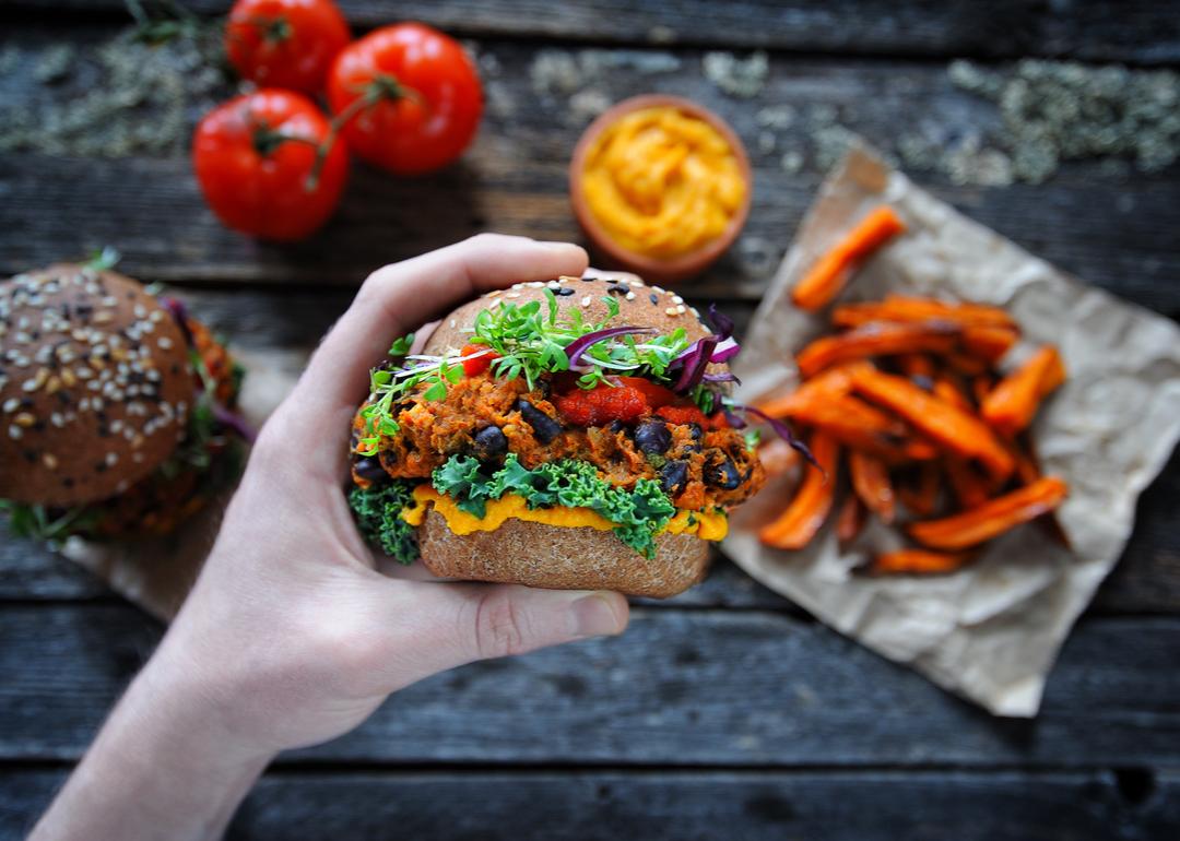A plant-based sandwich is held in front of a backdrop of other plant foods.