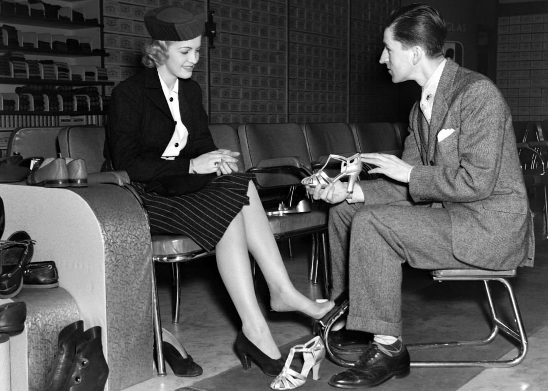 Shoe salesman helping woman try on a pair of high heels in the 1930s