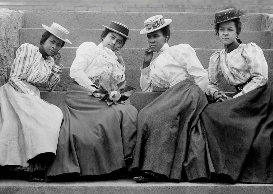 Four Black students in full skirts, blouses, and hats sitting on steps of Atlanta University.
