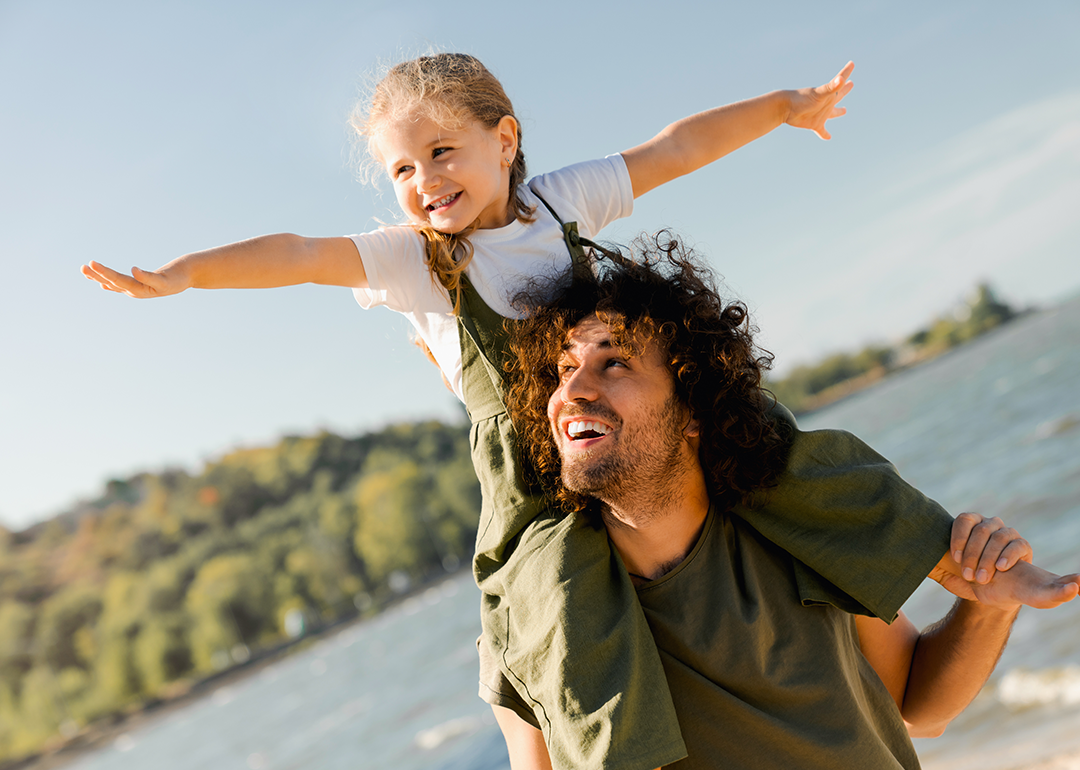 Father with daughter on shoulders walking at beach.