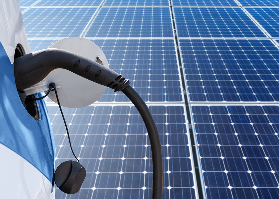 Close up of electric car with a connected charging cable on the background of solar panels.