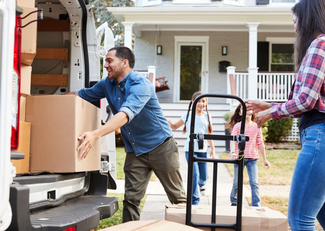 Family unloading boxes in front of suburban home.