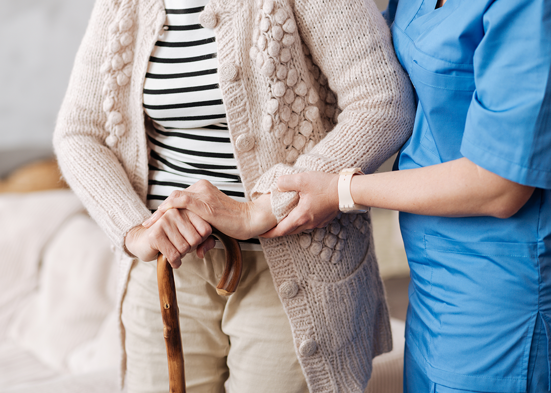 Nurse assisting senior woman with cane.