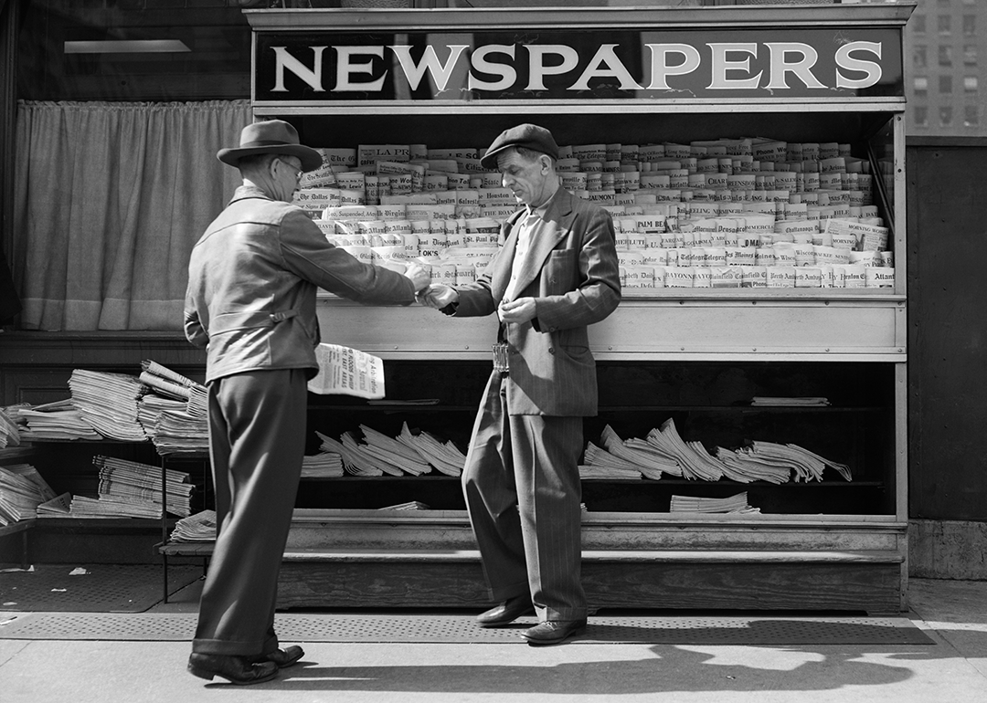 Man buying newspaper from vendor on sidewalk.