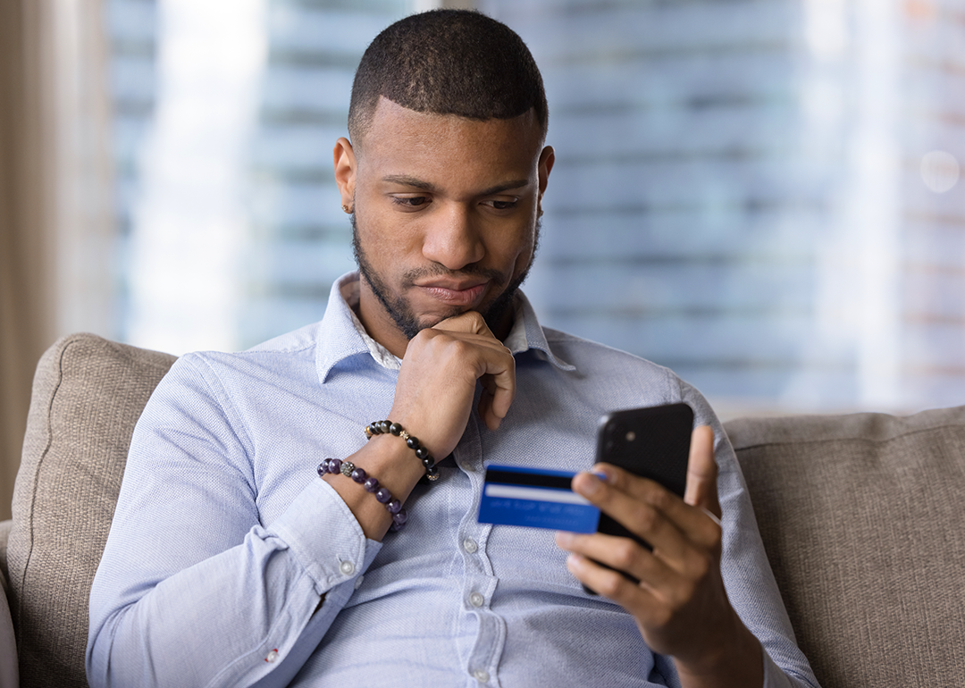 Man holding credit card and phone looking doubtful.