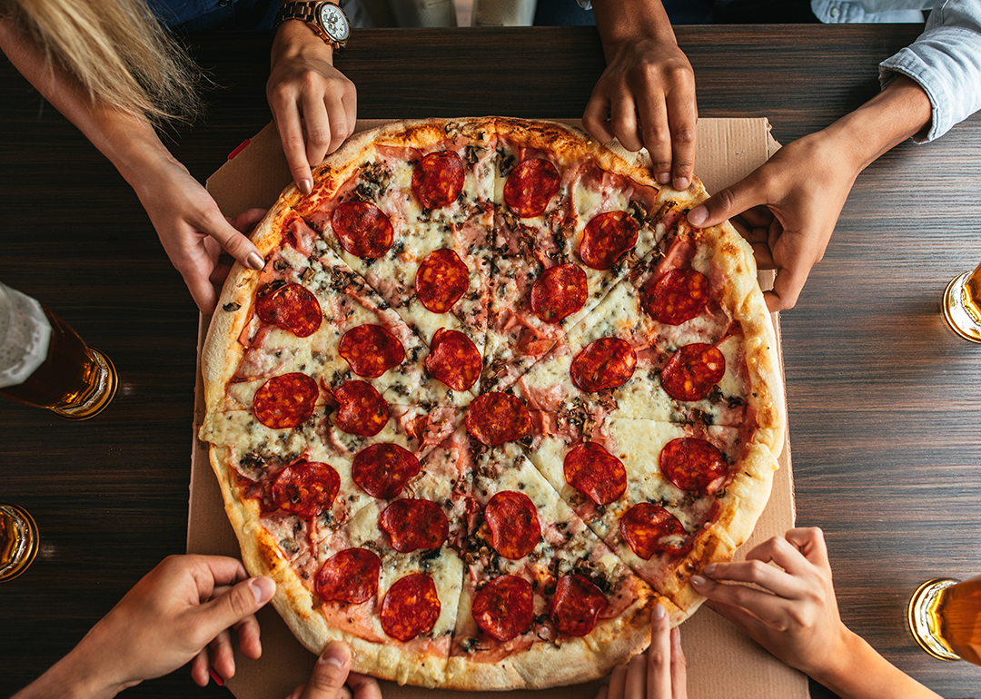 Group of people’s hands grabbing a slice of pizza.