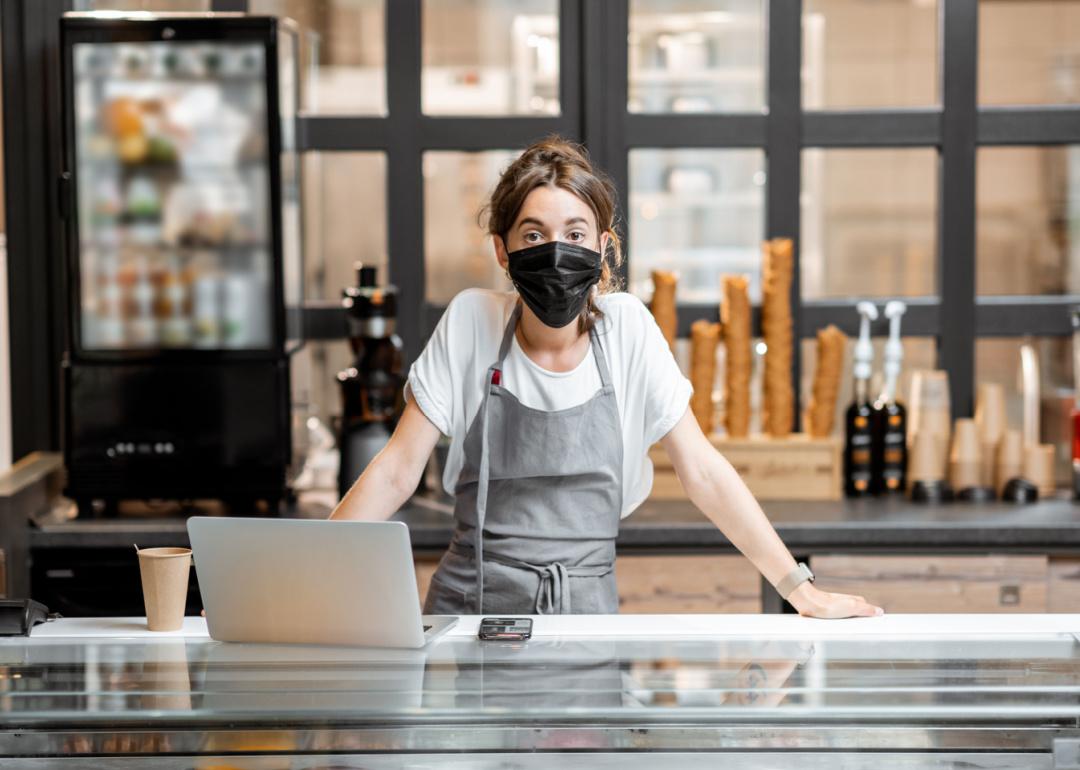 Cafe worker wearing mask with hands on counter.