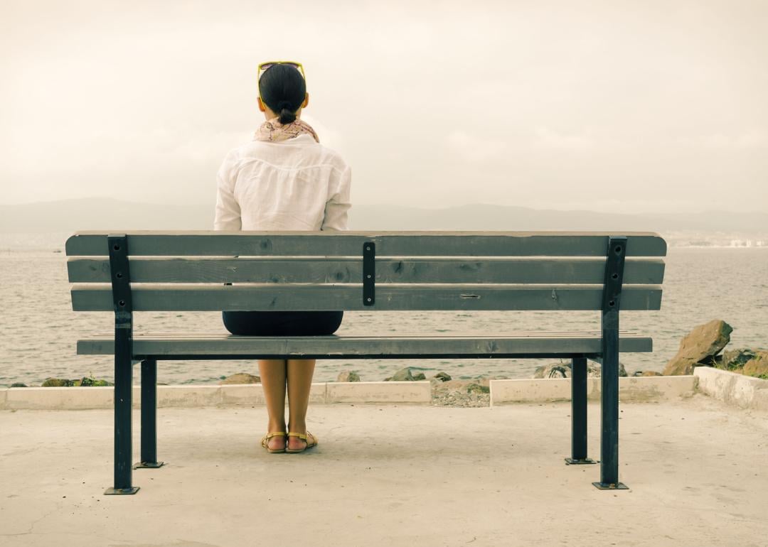 Woman sitting alone on a bench, looking out to the sea.