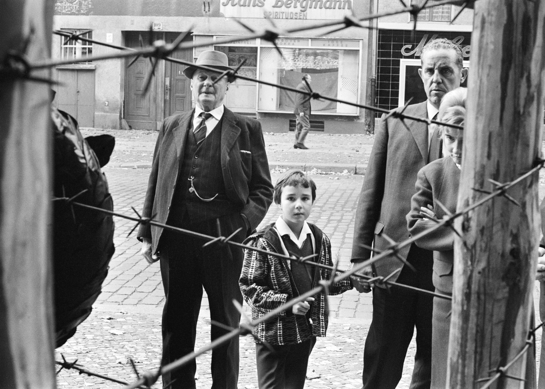 Citizens look through barbed wire fence during construction of the Berlin Wall.