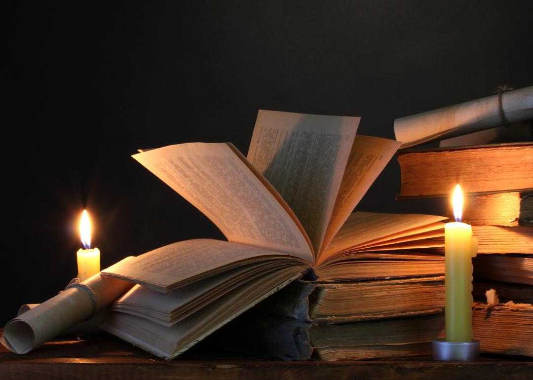 Two candles illuminate a stack of old books, with one on top open.