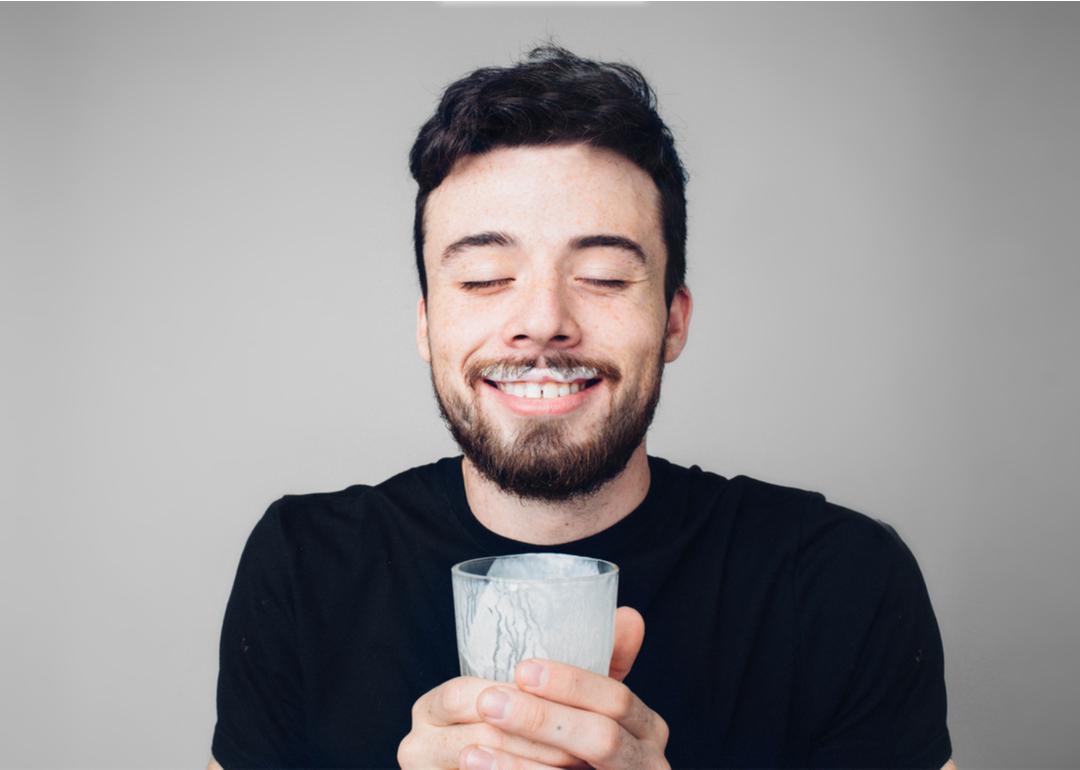 Man is drinking fresh glass of milk with a milk mustache, like the "Got milk?" ads