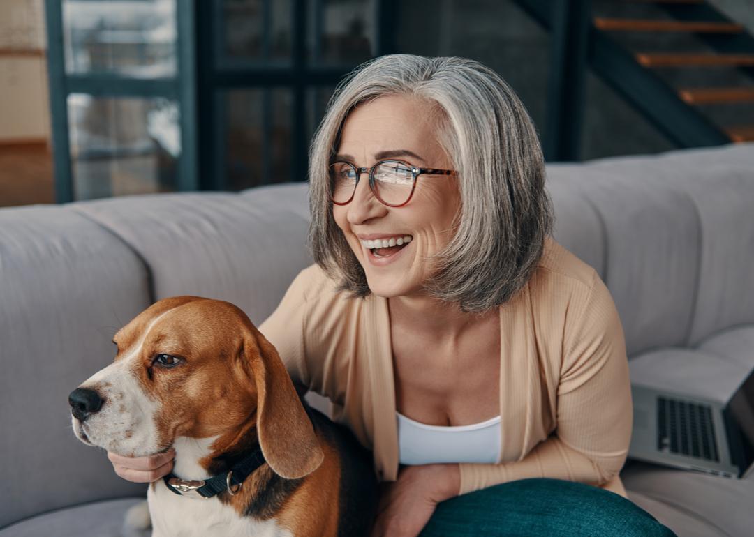 senior woman in casual clothing spending time with her dog while sitting on the sofa at home