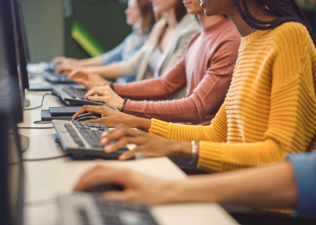 Closeup of a row of diverse workers on computers. The focus is on their hands.